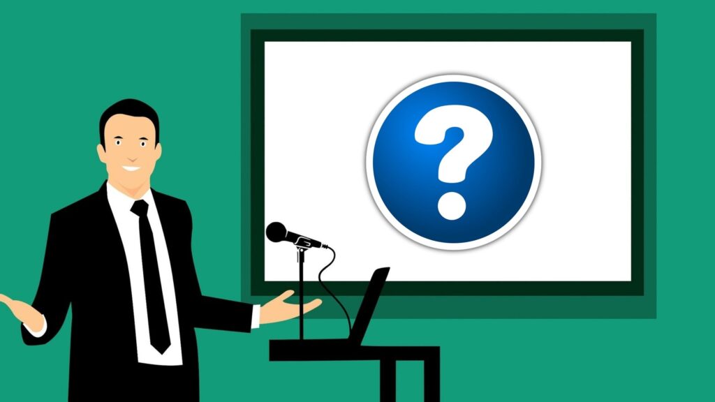 Image shows a man presenting on a screen that shows a big question mark